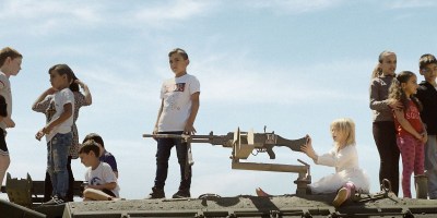 Kinder spielen auf einem Panzer, ein besonders unschuldig wirkendes Kind - blond im weißen Kleidchen - am Maschinengewehr